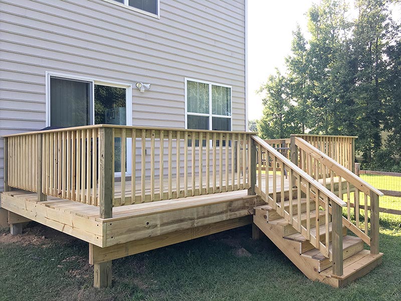 A wooden backyard deck with stairs attached to a house.