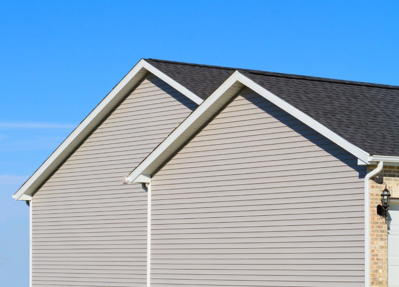 Two house gables with light-colored siding against a clear blue sky.