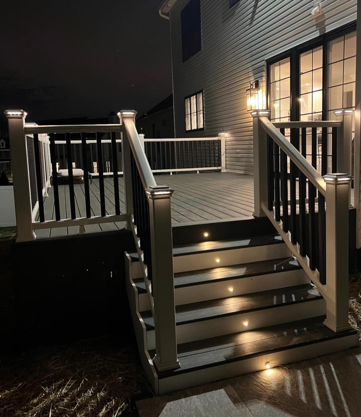 Elevated backyard deck with illuminated stairs and railing lights at night